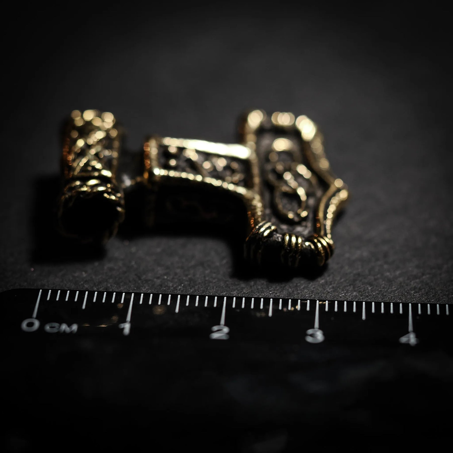 Bronze Thor's hammer pendant shown next to metric ruler for scale, displaying intricate Norse knotwork detail