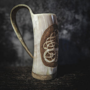 Handsnidad hornmugg i sidvy med krökd handtag. Urnes drakmotiv in graverat i djupt relief med pyrografi-detaljer. Organic horn i naturliga toner.
