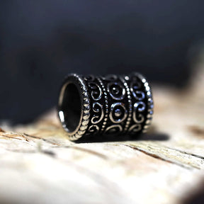 Närbild på skäggpärla Fimbula i mörkt stål med ornamentala spiralmönster, liggande på trä