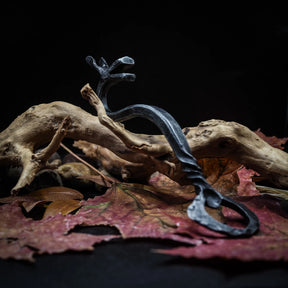 Älgflasköppnare av handsmedd återvunnen järn fotograferad på vädersliten ved och höstlöv, med naturlig mörk patina och detaljerade kornklingor.