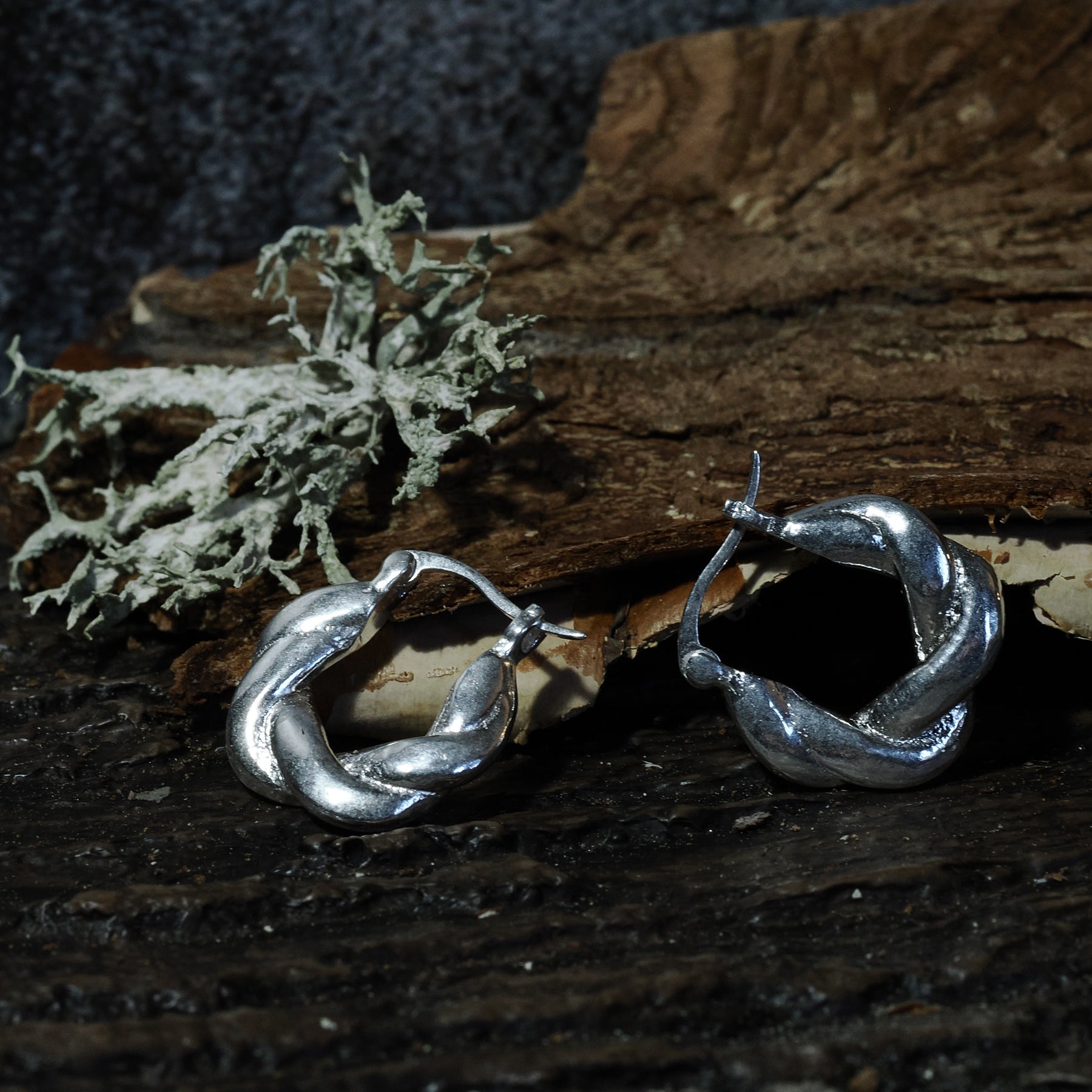 Par örhängen i silveröverlagring mässing på träbas, cirka 2 cm stora, visar flätmönster och rundad form