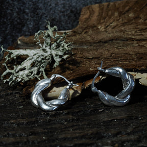 Par örhängen i silveröverlagring mässing på träbas, cirka 2 cm stora, visar flätmönster och rundad form