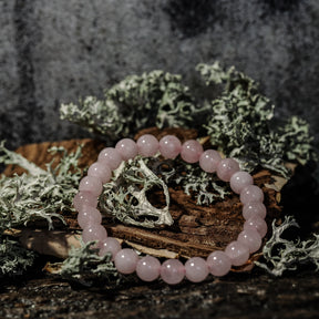 Armband stenpärlor - Tigeröga variant med rosenkvarts. Elastiskt armband med pastellrosa polerade stenpärlor på rustik träbas med mossbeväxt stenbackgrund. Pärlorna har soft translucent kvalitet.