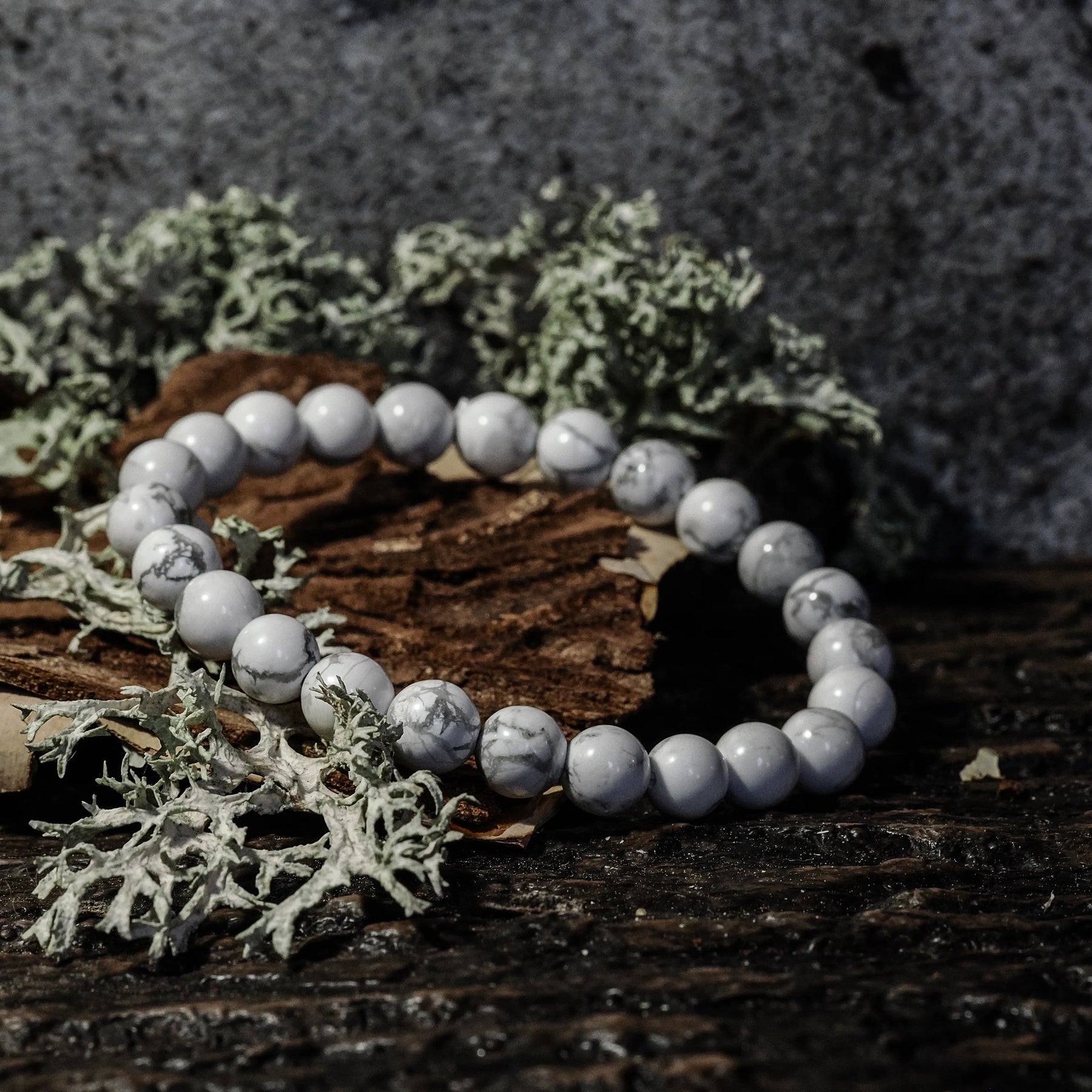 Armband stenpärlor - Tigeröga variant med vit marmor. Elastiskt armband med vita polerade pärlor med naturliga svarta ådror på rustik träbas och mossbeväxt stenbackgrund.