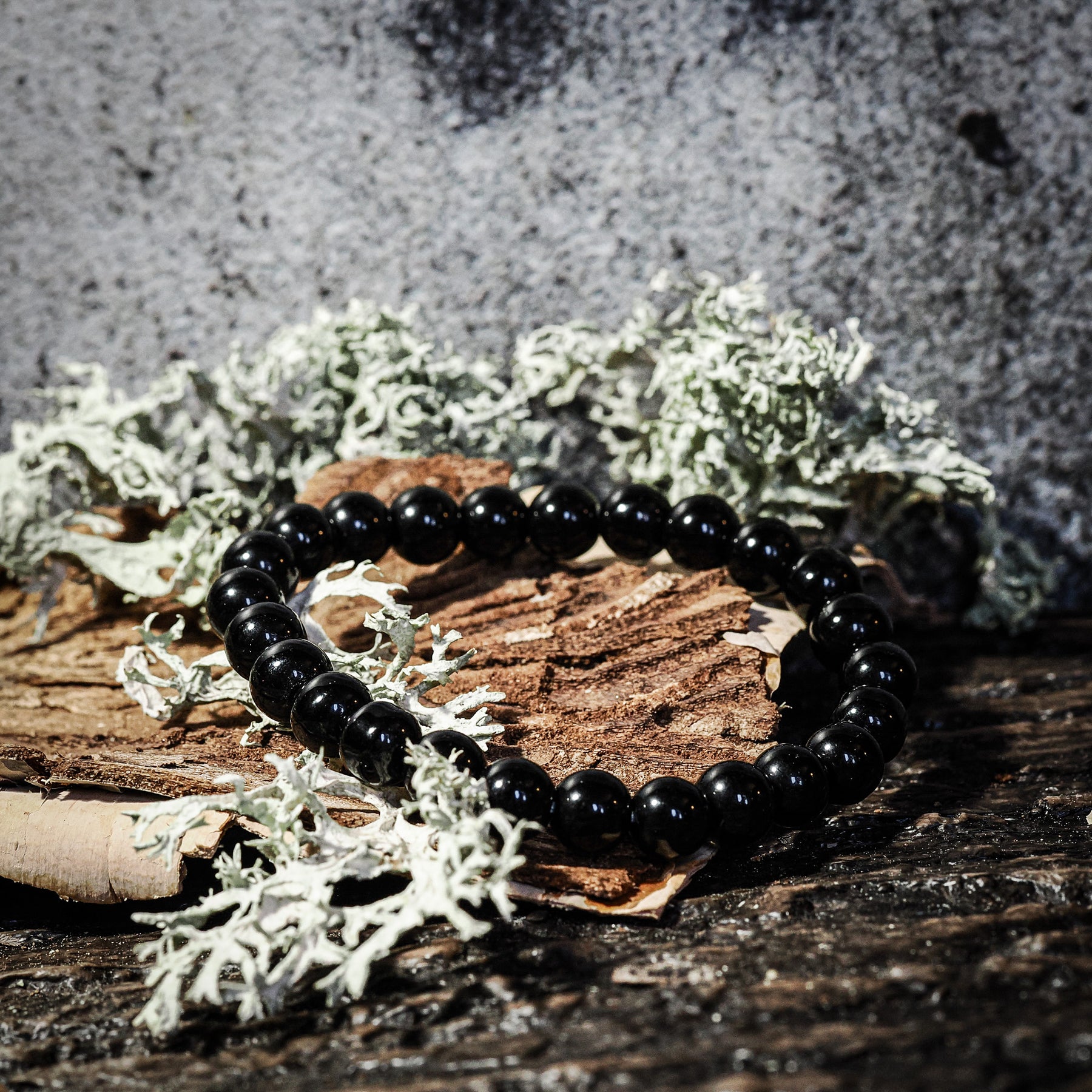 Armband stenpärlor - Tigeröga variant med svart turmalin. Elastiskt armband med djupsvarta polerade stenpärlor på rustik träbas med mossbeväxt stenbackgrund.