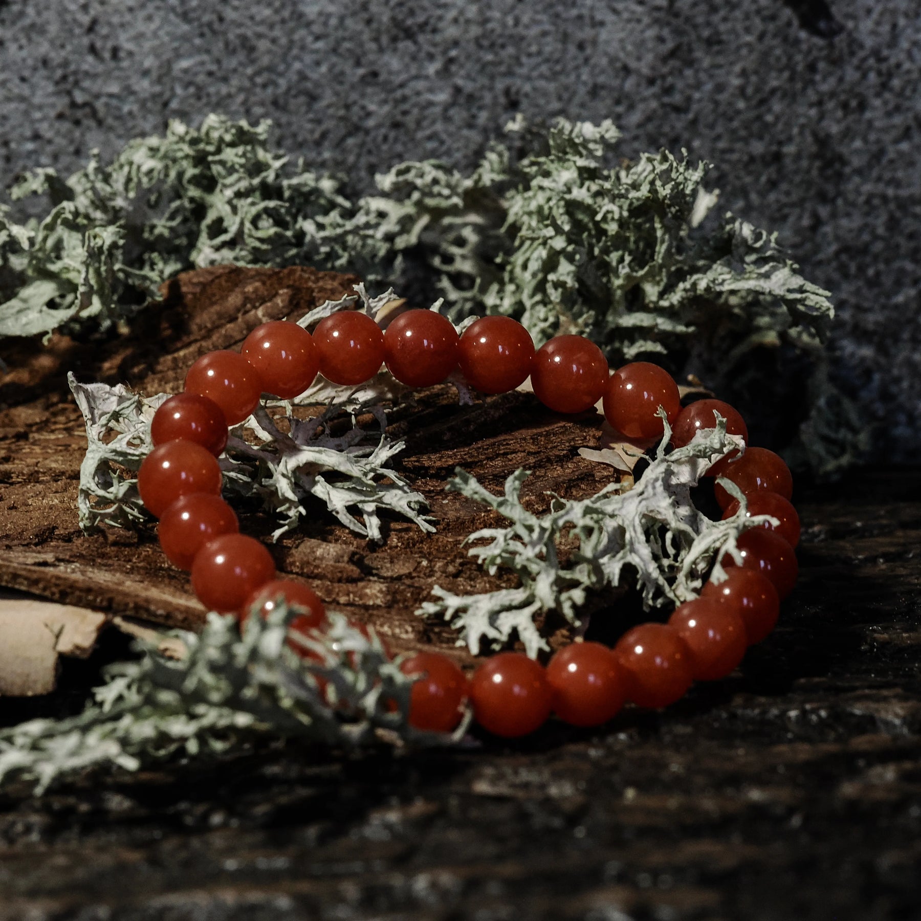 Armband stenpärlor - Tigeröga variant med karneol. Elastiskt armband med röda polerade karneol-pärlor på rustik träbas med mossbeväxt stenbackgrund.