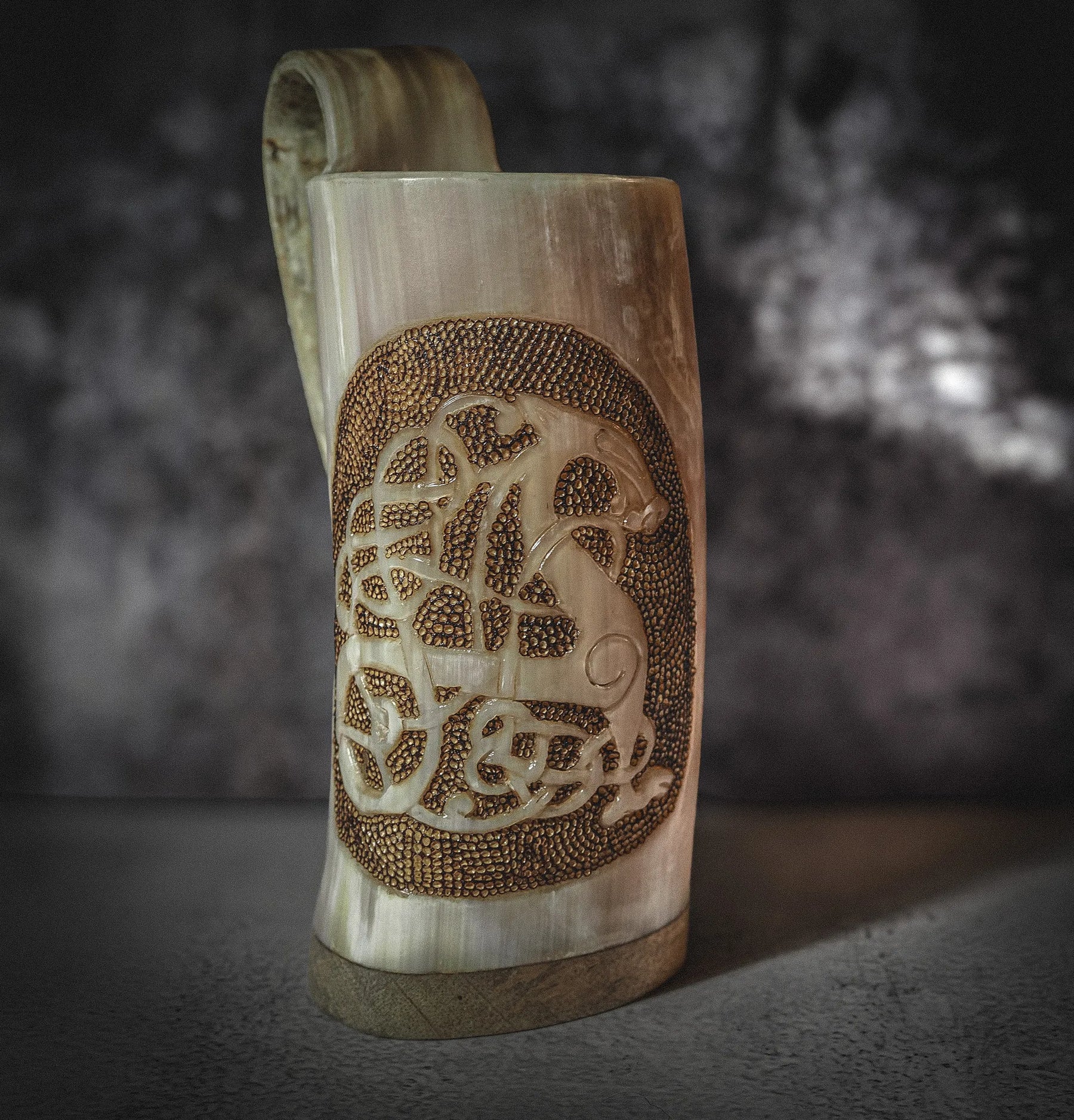 Handsnidad hornmugg visad från sida med djupskuren Urnes drakmotiv och pyrografi. Organic horn i kräm- och brunton med handtag synligt.