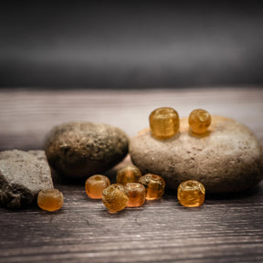 Bärnstensfärgade glaspärlor i flera storlekar på mörk träyta med natursten, visar handgjord kvalitet och varm guldgul färg