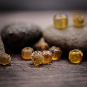 Amber-coloured glass bead – several beads among stones on a wooden surface