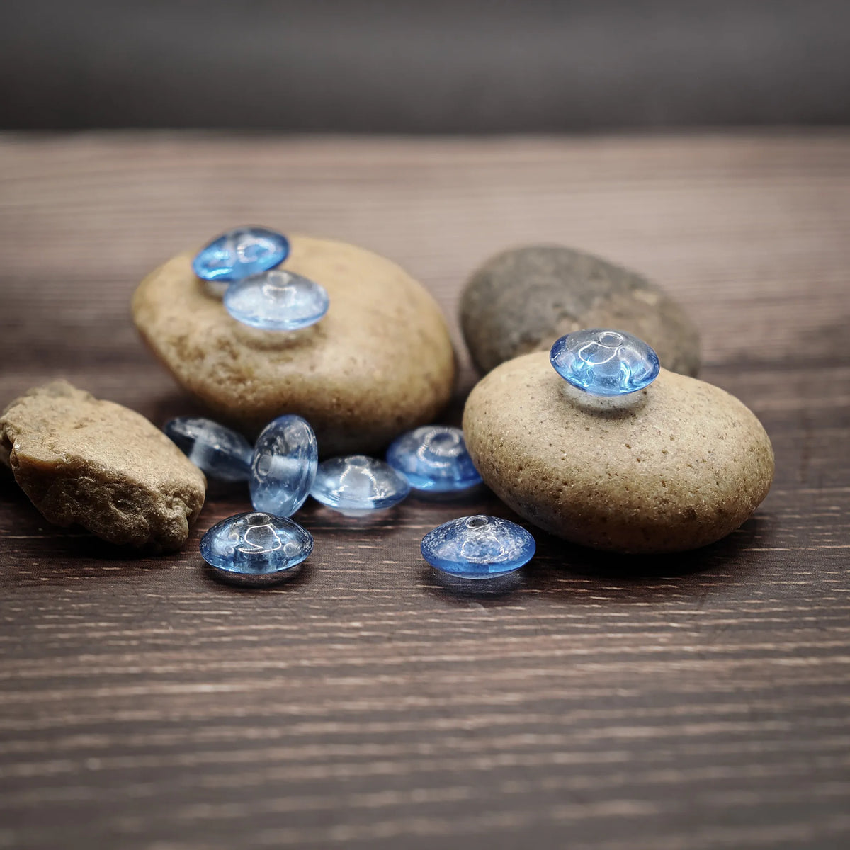 Ljusblå linsformade glaspärlor, 10mm, transparenta med ett millimeters hål, fotograferade på trä- och stenunderlag