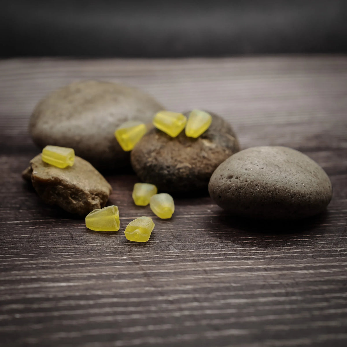 Citrongula glaspärlor på natursten, glansiga och transparenta. Små pärlor för smycken och bånd, på trämönstrad yta.