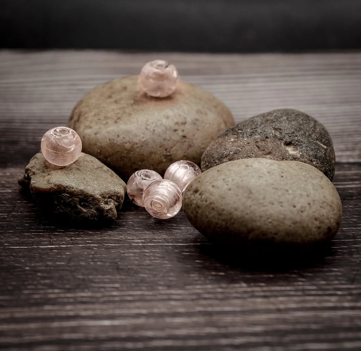Tre ljusrosa transparent glaspärlor på stenar och trä, med perlemor-glans och naturlig bakgrund
