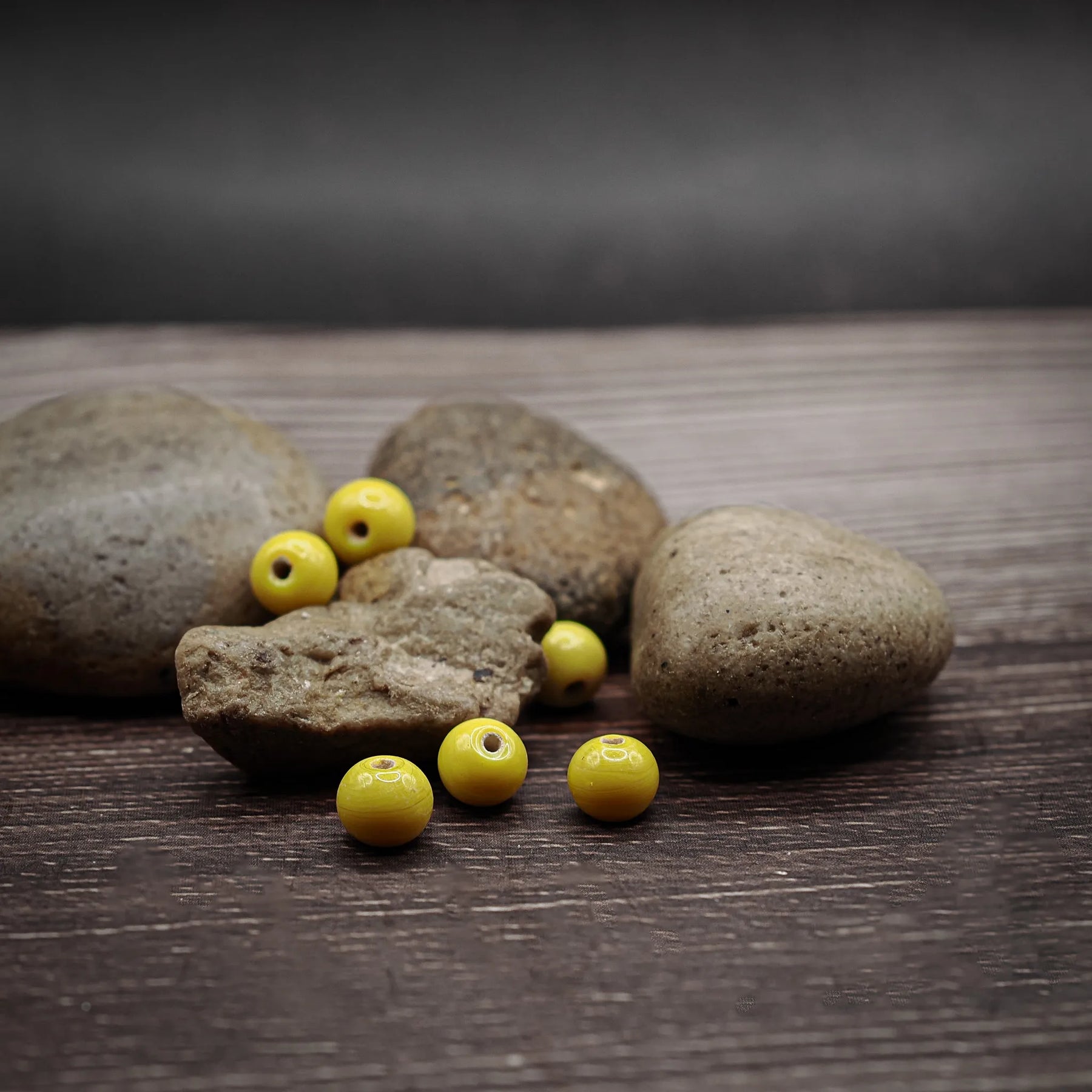 Liten gul glaspärla (alternativ vy) - visning av handgjorda glasperler i gulfärgad nyans på naturlig stenbackgrund