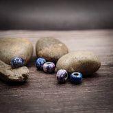 Fyra blålila glasspärlor med varierande mönster (prickar, ränder), fotograferade på trä med stenar