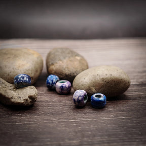 Fyra blålila glasspärlor med varierande mönster (prickar, ränder), fotograferade på trä med stenar