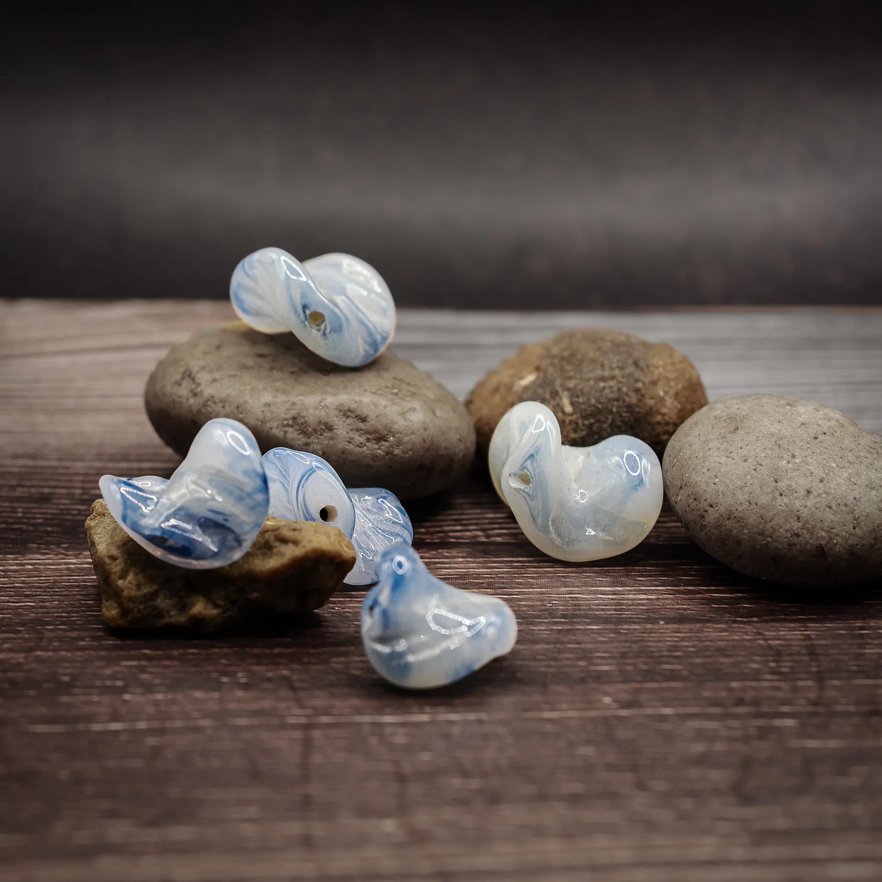 Vit och blå glaspärla från Ragnarök-serien - duplikat foto. Samma fem pärlor visar hopvikta geometriska former med blå mönster inuti vitt glas.