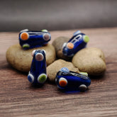 Fem mörkblå formade glasspärlor med färgade prickar (orange, gul, grön, vit), fotograferade på trä med stenar