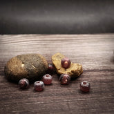 Mauve-colored glass beads, small spherical beads approximately 5 millimeters in diameter. Handmade beads in muted purple-grey tone with matte finish. Several beads shown on natural wooden base with visible holes for threading.