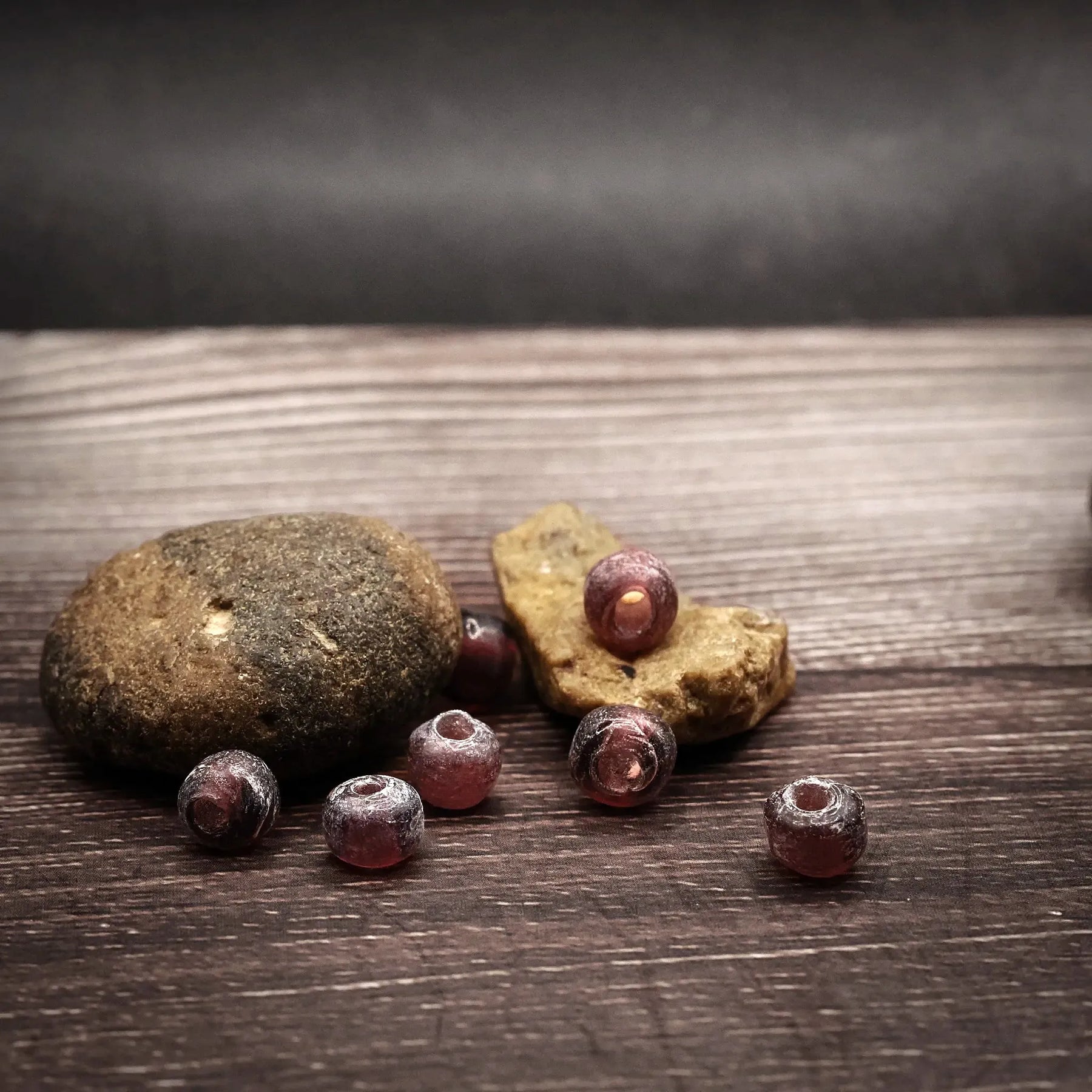 Mauve-colored glass beads, small spherical beads approximately 5 millimeters in diameter. Handmade beads in muted purple-grey tone with matte finish. Several beads shown on natural wooden base with visible holes for threading.