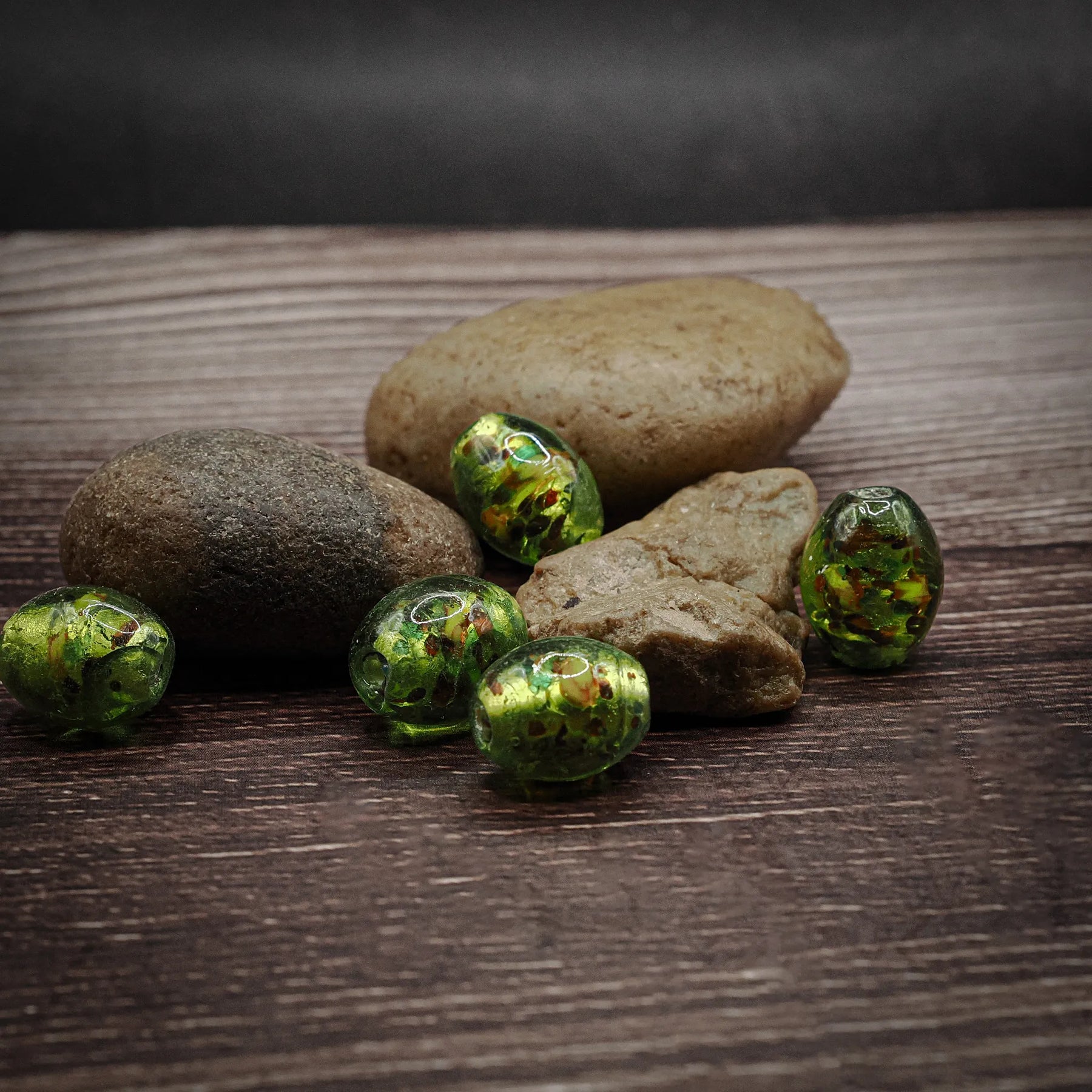 Fem gröna glaspärlor med oval form på träyta. Vikingatida pärlor associerade med Ragnarök-temat, hand-gjorda med mässingsögonknappar.