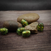 Fem gröna glaspärlor med oval form och mässingsögonknappar på träyta. Vikingatida pärlor cirka 12mm i diameter med handblåst glasfinish.