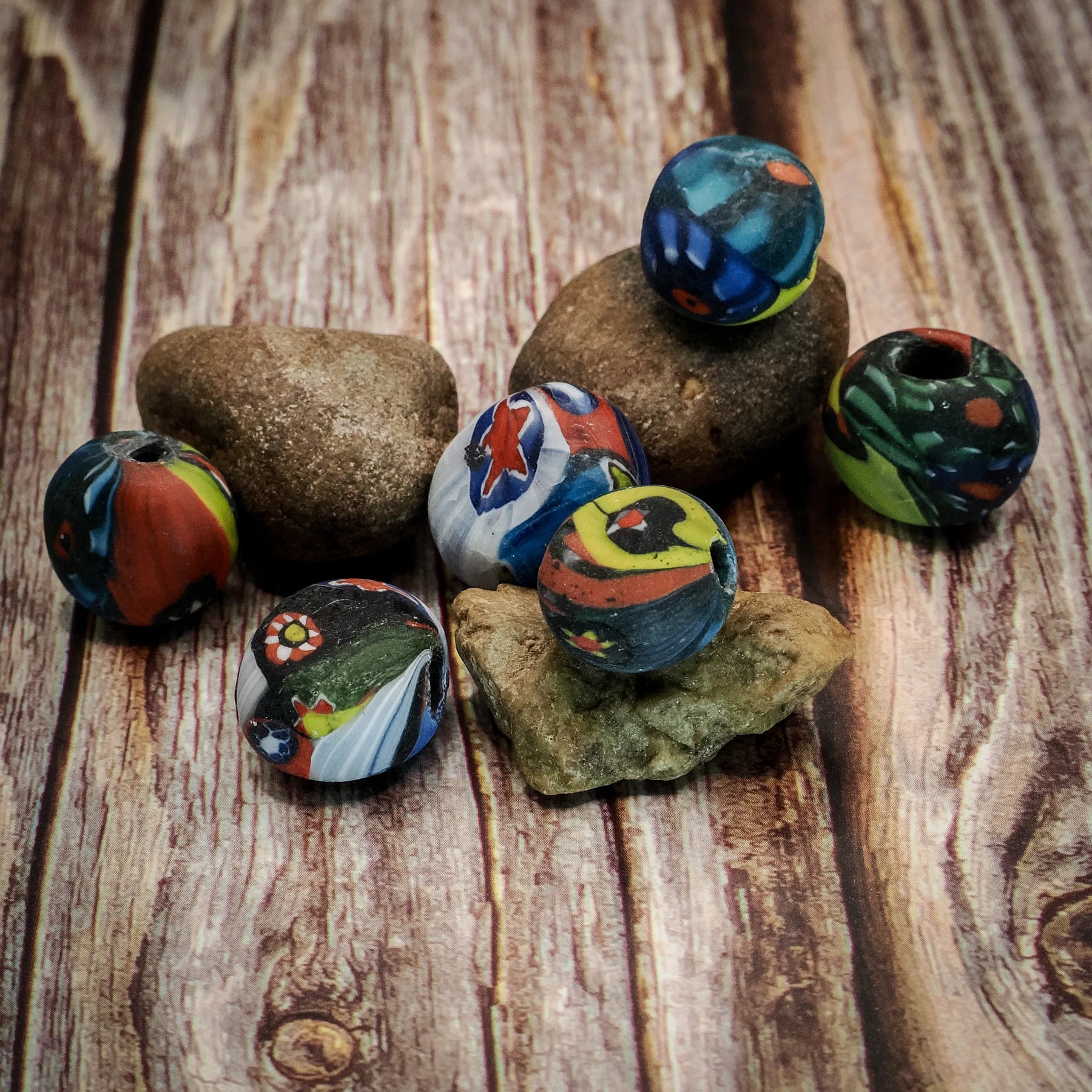 Flerfärgad glaspärla 07700119 på sten med målat norsk motiv. Pärlan är 10x15mm med 3mm hål och visar detaljerade Viking-ansikten i blått, grönt, gult och orange.