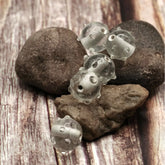 Fyra transparenta handgjorda glaspärlor med upphöjda prickar, uppträdda på tråd mot stenar