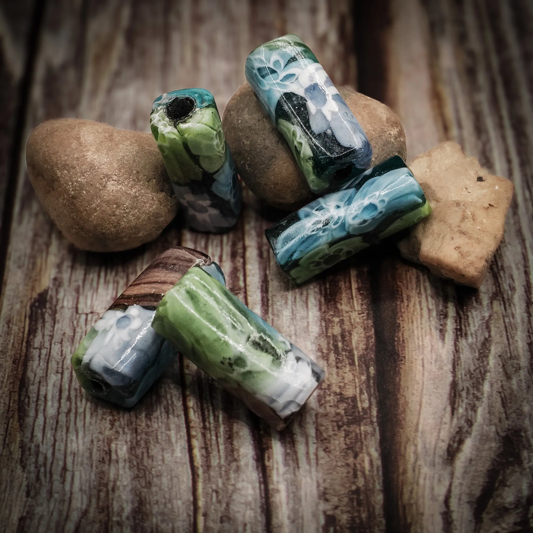 Flerfärgad rektangulär glaspärla med målat blom- och geometriskt motiv i grönt, blått och vitt. Pärlan är cirka 25x10mm med detaljer som passar Viking-smycken.