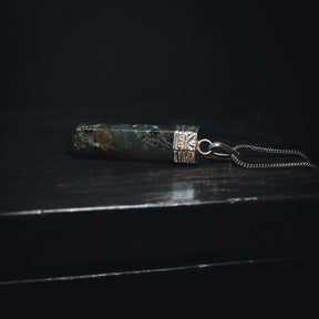 Labradorit-hänge med iriserade blå-gröna ljusblixtar. Polerad kristallsten med metallfattning och ögonkrok. Kedja säljs separat. Studio-produktfoto på vit bakgrund.