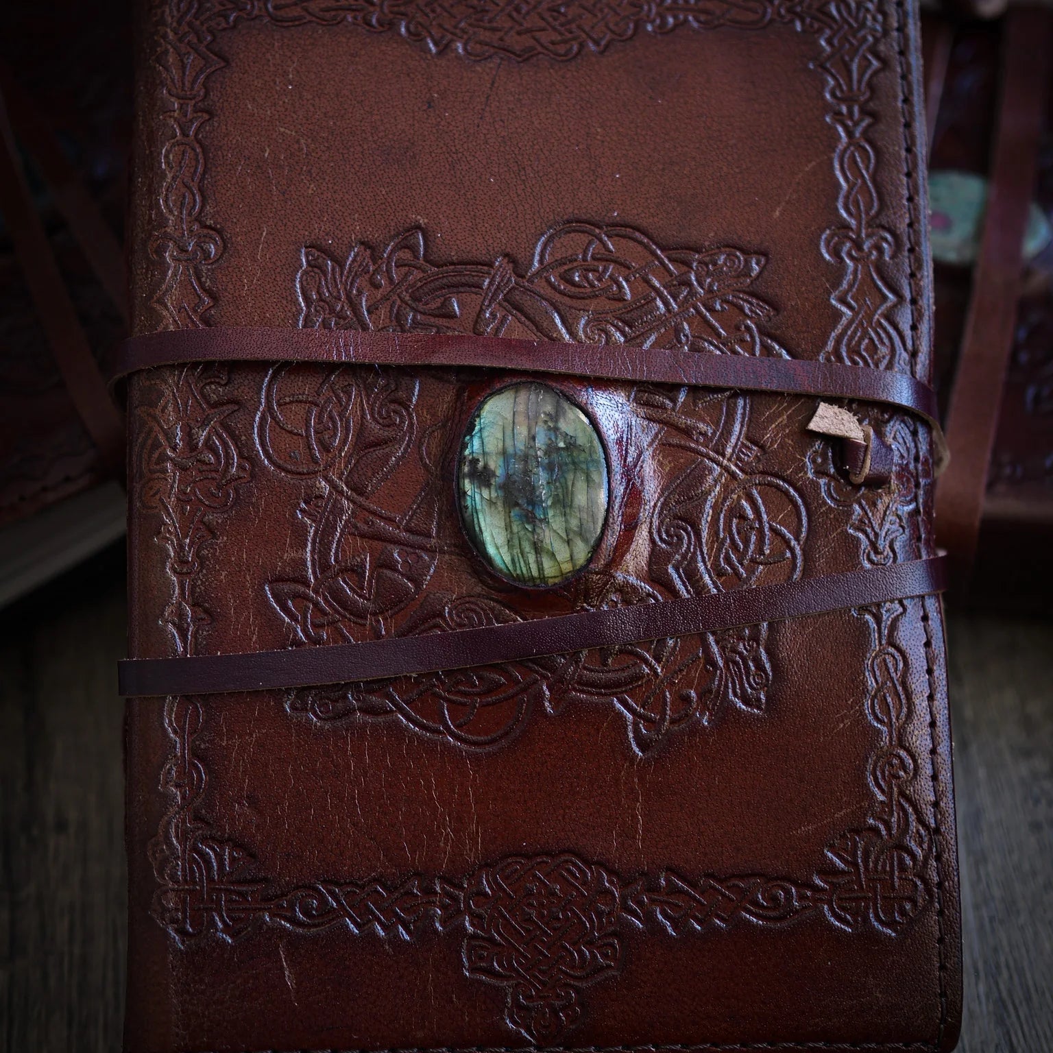 Handgjord läderbok Kristall i medium med labradorit-sten. Burgundibrunt läder med präglad vikingkant, blågrön labradorit-sten med iriserande glans i metallfattning och brunt läderband.
