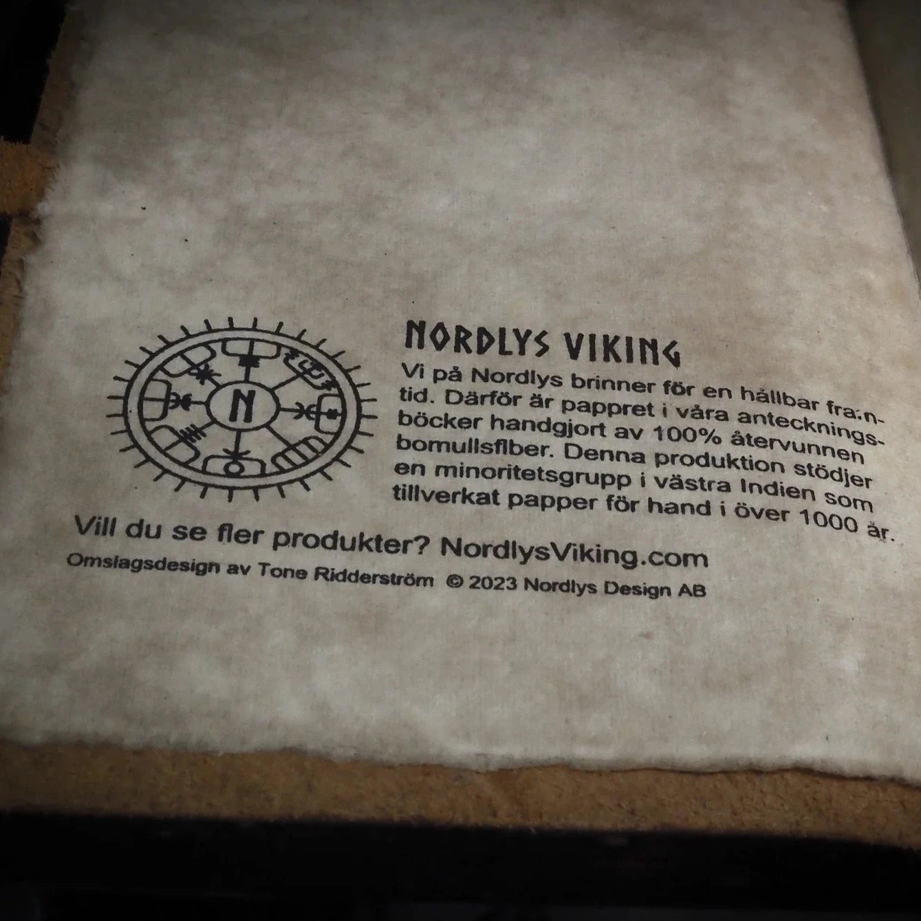 Bakre omslag med Nordlys Viking märke och information om hållbar och rättvis produktion på handgjort bomullspapper
