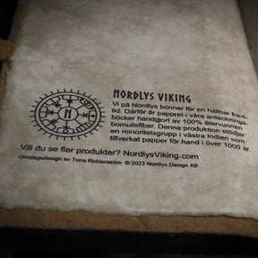 Bakre omslag med Nordlys Viking märke och information om hållbar och rättvis produktion på handgjort bomullspapper