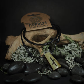 Handgjord runhalsband i ben på svart lädersnöre med Tiwaz-runan, visad på mannekäng med NORDLYS märke, stiliserad med naturliga material som dried moss och stenar.