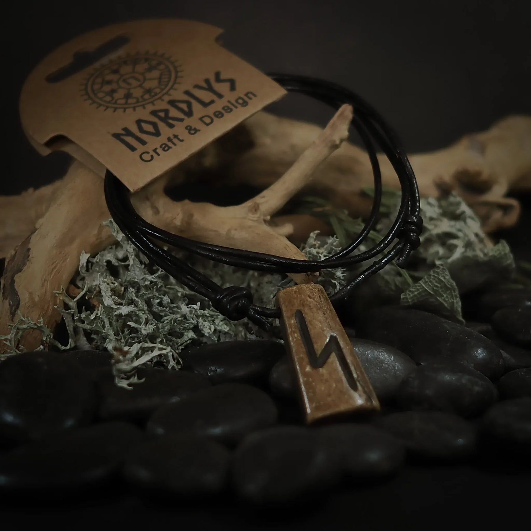 Handgjord runhalsband i oxben med svart lädersnöre. Runitskriften är tydligt inristad i det ljusa benets. Produkten är styladpå naturlig bakgrund för att framhäva dess autentiska, nordiska karaktär.