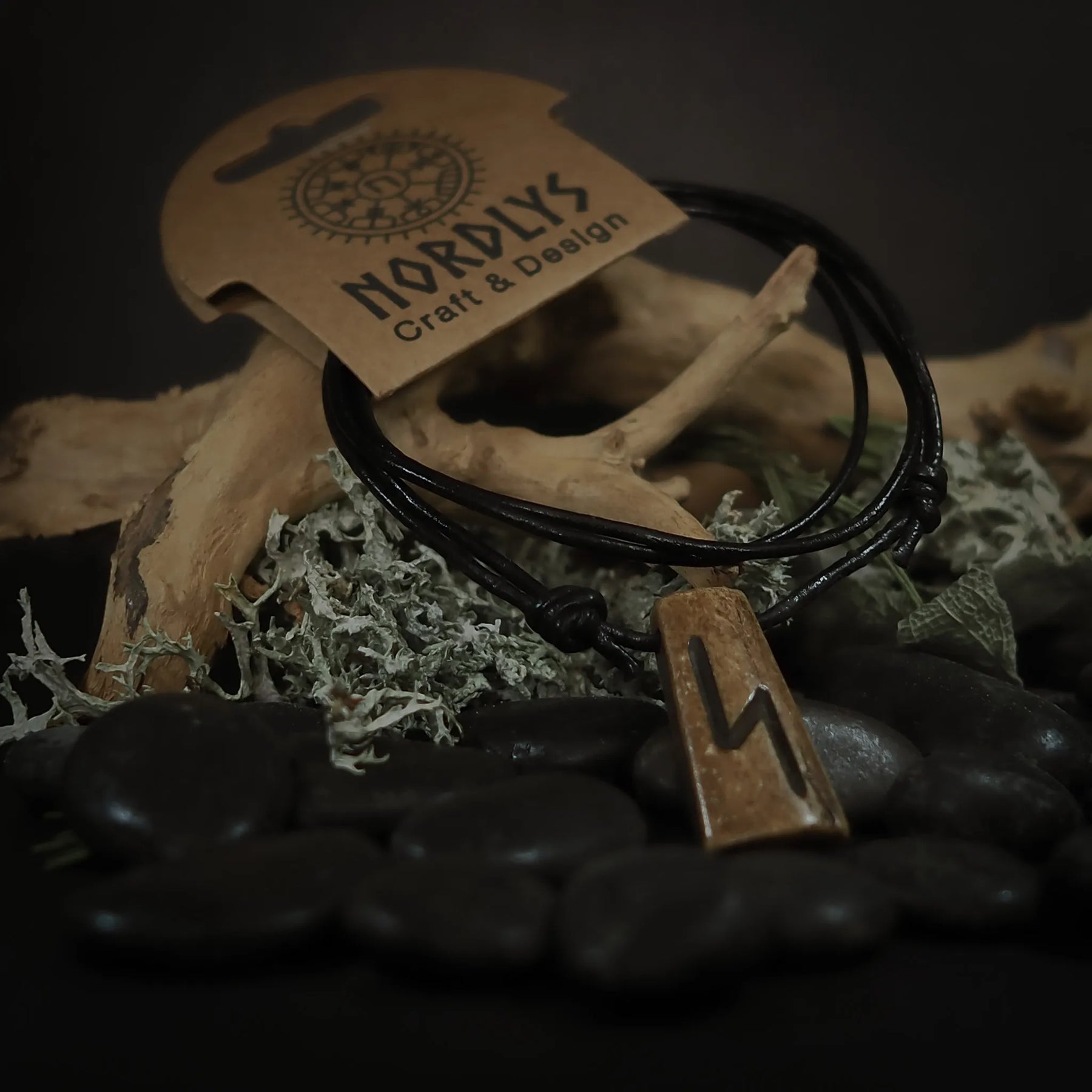 Runhalsband i oxben med Perthro-runan inristad. Hänget är uppsatt på svart lädersnöre och presenteras på en rustik naturlig bakgrund med mossa och gräs. Produkten visar nordisk hantverk och tradition.