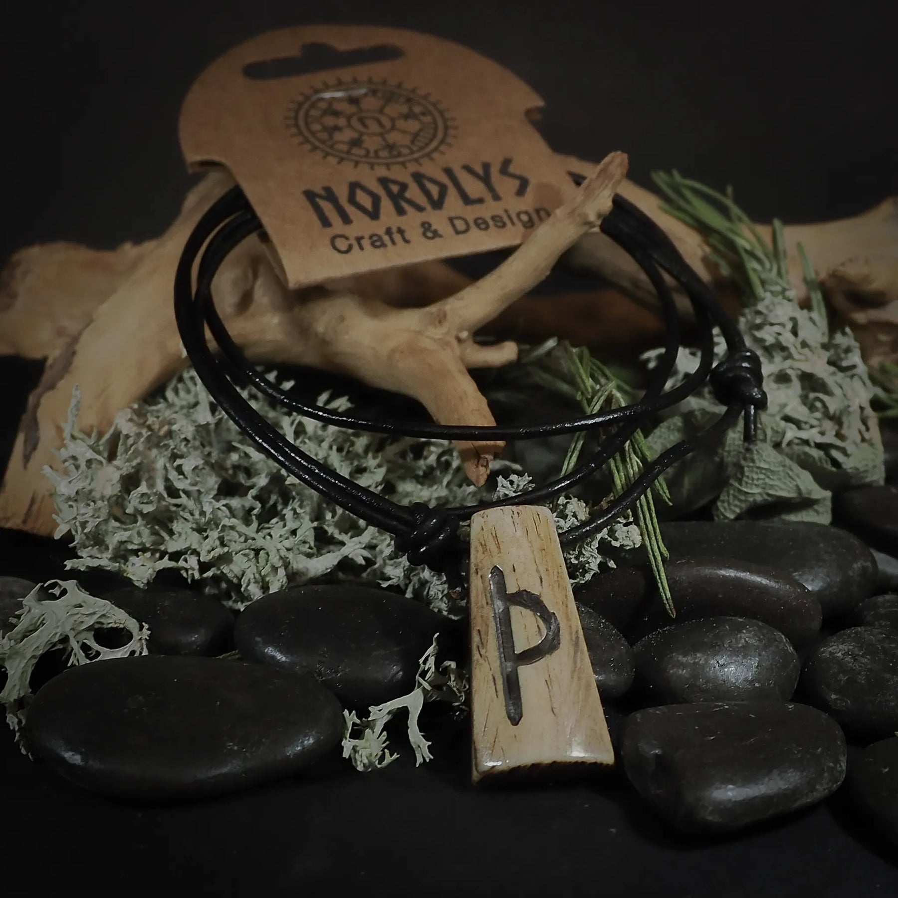 Runhalsband med Perthro-runan inristad i oxben. Pendant är monterad på svart lädersnöre. Fotografi visar detaljerna i det handskurna runasymbolet på den ljusa, naturliga benslutan.