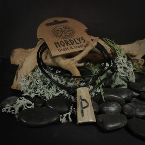 Närbild av Perthro-runan inristad i oxbenets pendant. Runasymbolet är tydligt och väl utfört i det ljusa benets. Svart lädersnöre håller hänget. Fotografi framhäver den hantvarksmässiga kvaliteten.