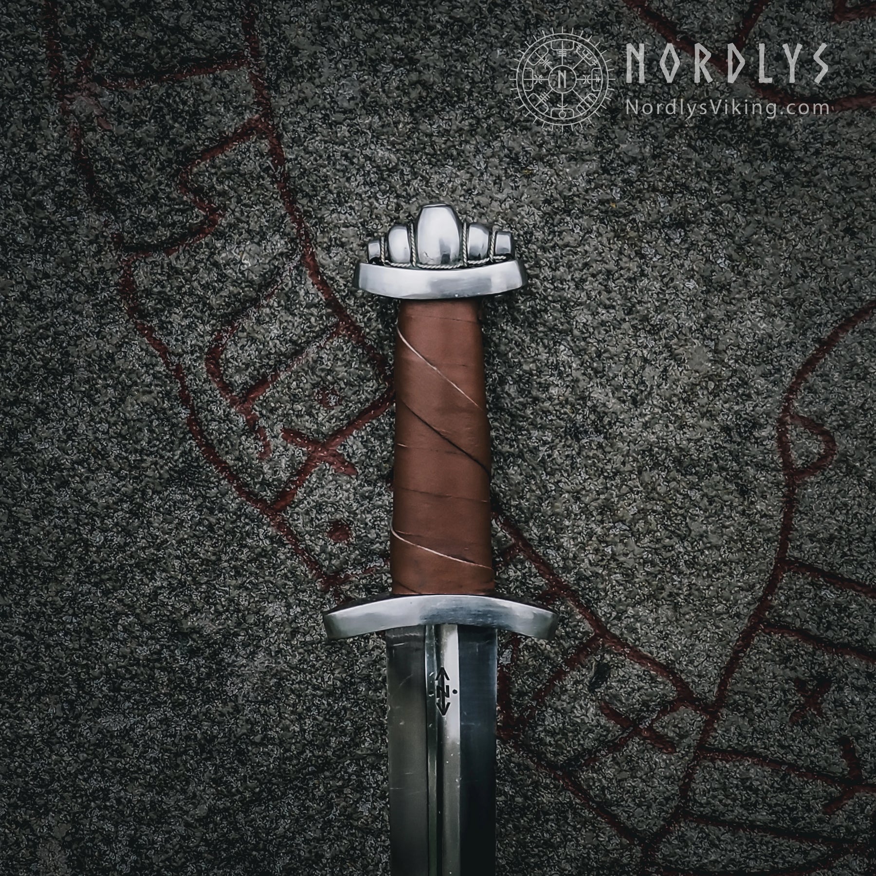 Vikingasvärd med femlobad pommel fotografi mot gröngrå textilbakgrund. Autentisk design från Nordlys Viking.