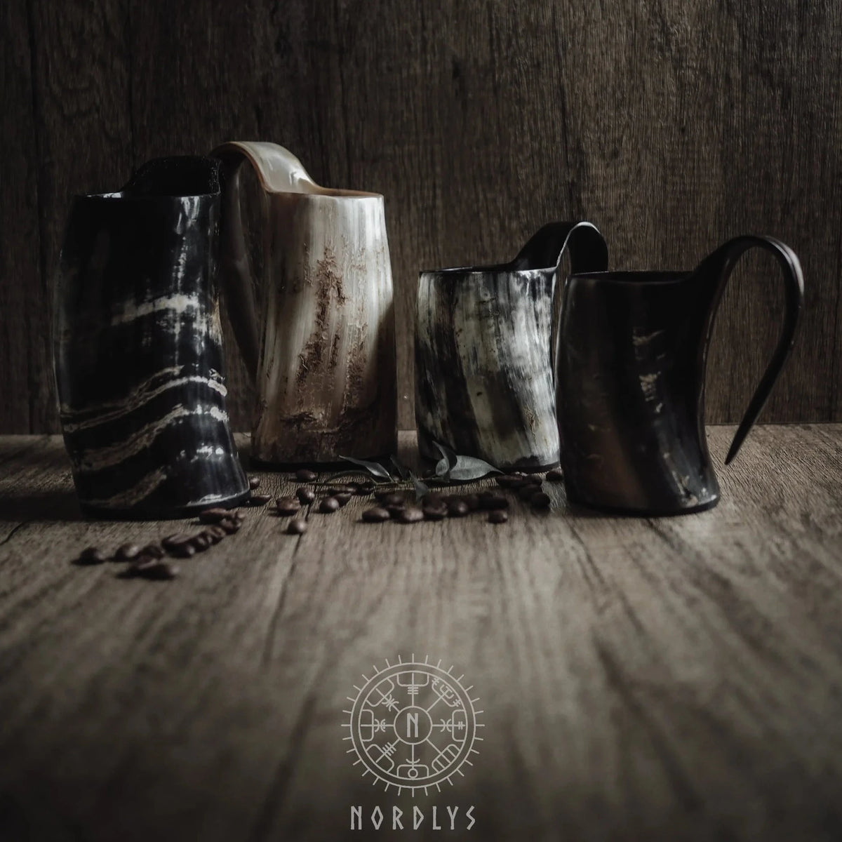 Tre mörka hornmuggar arrangerade på rustik träyta med kaffebönor och Nordlys-logotyp. Visar hornmaterialets naturliga textur och färg.