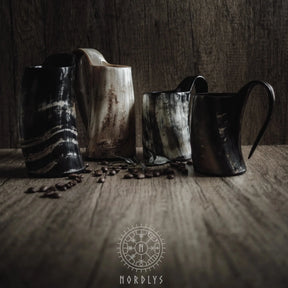 Tre mörka hornmuggar arrangerade på rustik träyta med kaffebönor och Nordlys-logotyp. Visar hornmaterialets naturliga textur och färg.