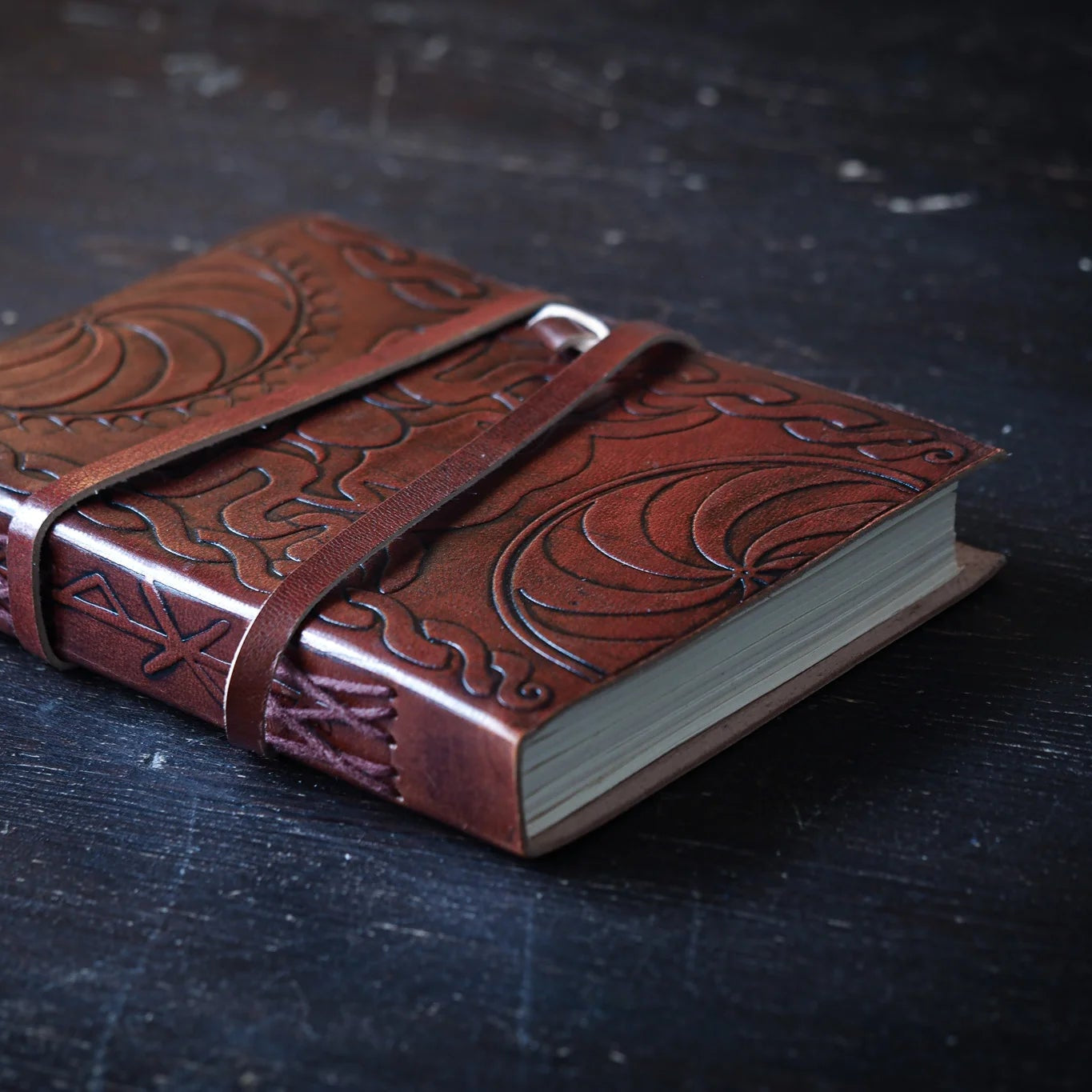 Leather notebook spine with detailed embossed Viking serpent and Triglav-inspired dragon designs, viewed at angle with binding straps visible