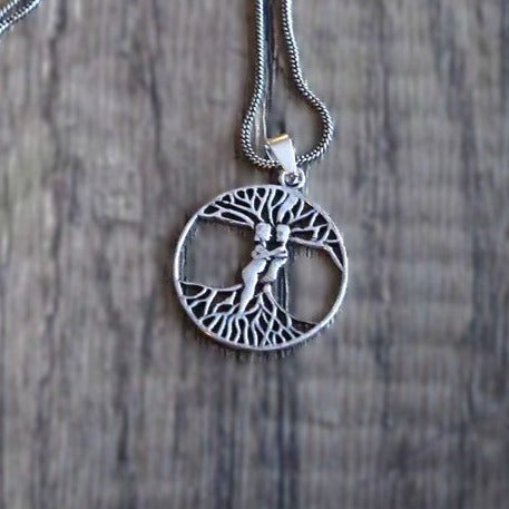 Silverkedja med träd-amulett som visar Yggdrasil-motivet med symmetriska rötter och grenar, fotograferad på träbakgrund.