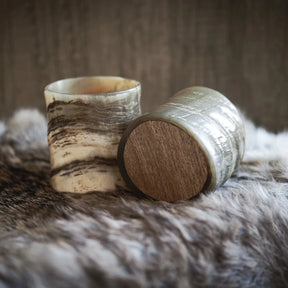 Whiskyglas i naturlig horn med organisk textur och träbas, presenterade på pelskudde