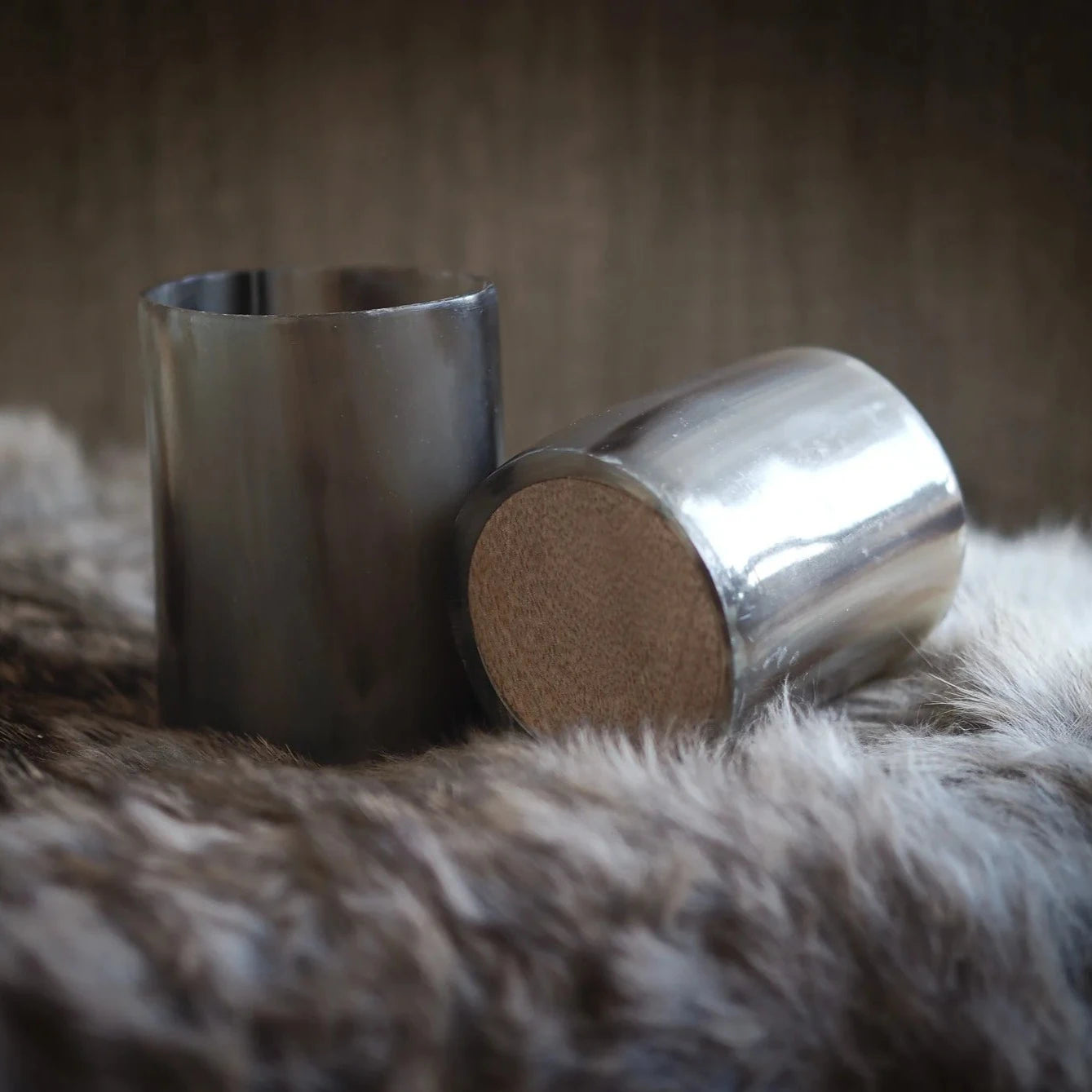 Två hornglasögon för whisky fotograferade tillsammans, visar träbotten och polerad kant mot neutral textilbakgrund.
