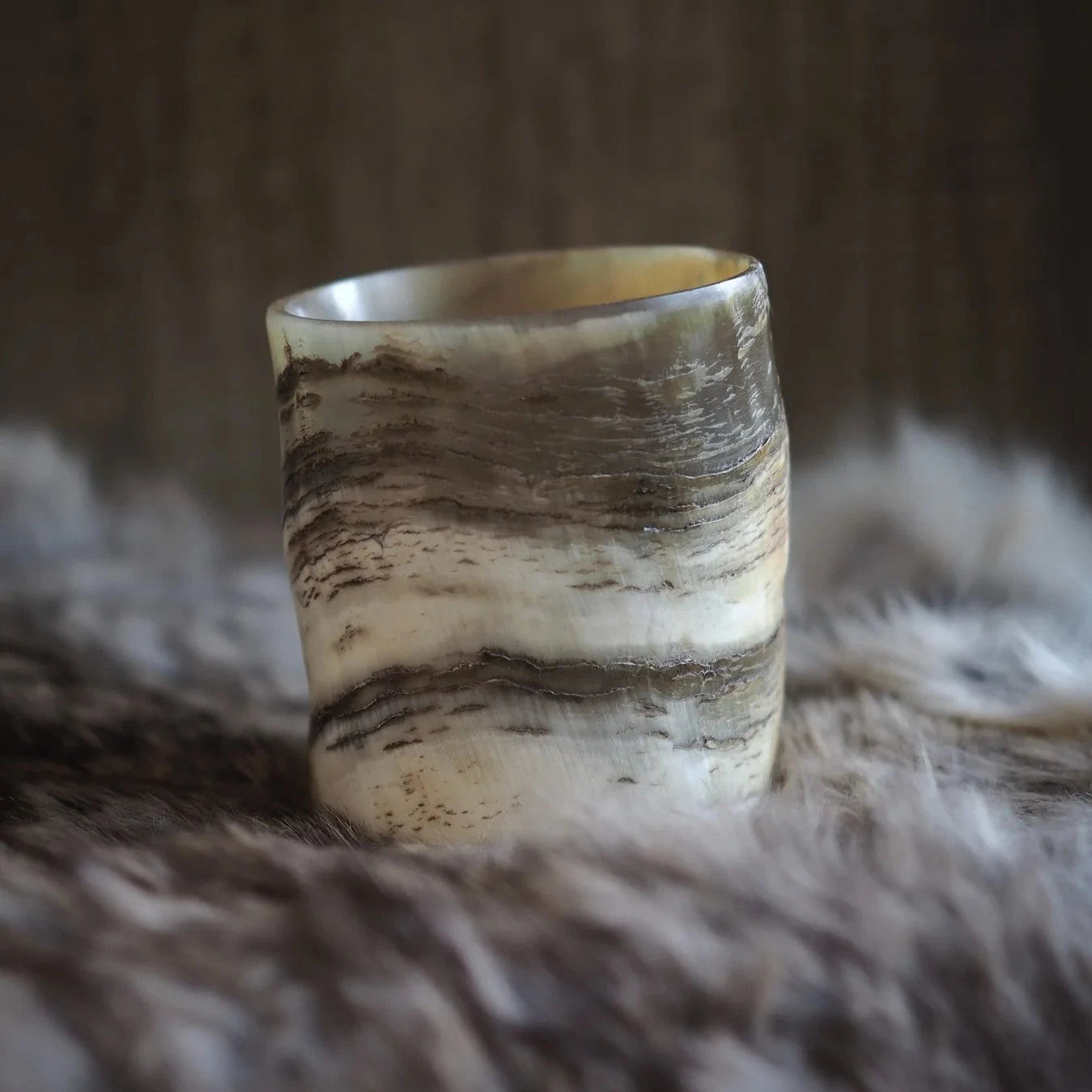 En naturlig hornglasögon för whisky med organiska ådringar och randiga mönster i beige och brunt, fotograferad mot neutral textilbakgrund.