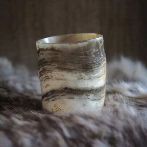 En naturlig hornglasögon för whisky med organiska ådringar och randiga mönster i beige och brunt, fotograferad mot neutral textilbakgrund.