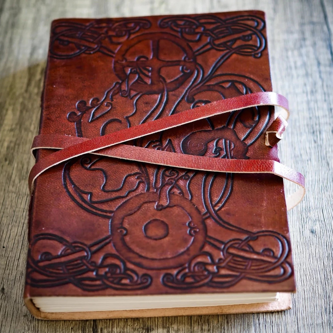 Närbild på läderanteckningsbok med präglade vargar och keltiskt mönster, stängd med läderrem