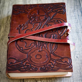 Närbild på läderanteckningsbok med präglade vargar och keltiskt mönster, stängd med läderrem