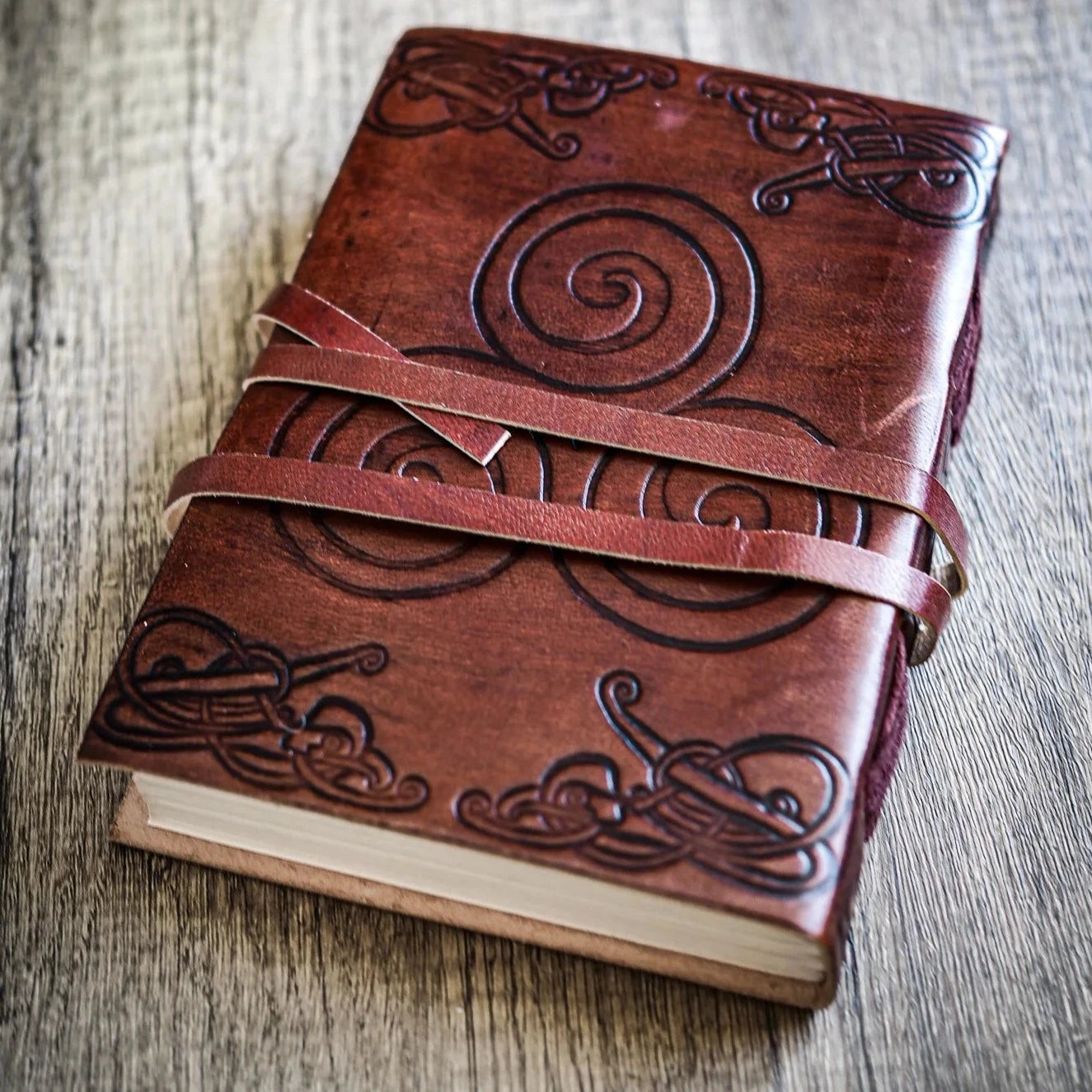 Baksidan av läderanteckningsbok med präglade spiralmönster och keltiska knutar, stängd med rem