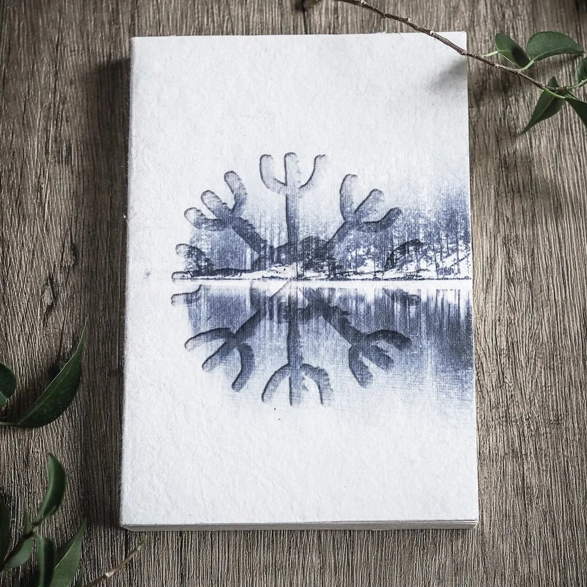 A6 målarbok, Skyddsruna. Öppen uppslag visar Aegishjalmur-rune med speglad skogsmotiv. Fotografi på trä med växter.